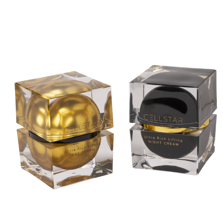 Gezeigt werden die beiden luxuriöse Cellstar-Produkte Ultra Rich Lifting Day Cream und Ultra Rich Lifting Night Cream in stilvollen Tiegeln. Links befindet sich die Ultra Rich Lifting Day Cream in goldenem Tiegel, rechts die Ultra Rich Lifting Night Cream in edlem Schwarz. Diese hochwertigen Anti-Aging-Cremes sind für eine intensive Pflege tagsüber und über Nacht konzipiert, um die Haut zu straffen, Falten zu reduzieren und die Gesichtskontur zu festigen.